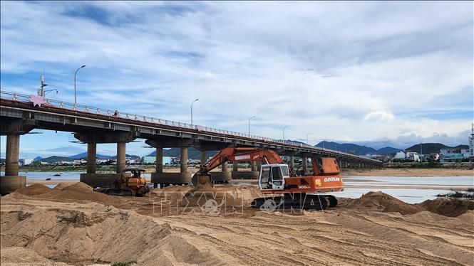 Cơ quan chức năng sử dụng máy đào để vun cát, gia cố chân cầu. Ảnh: Sỹ Thắng - TTXVN