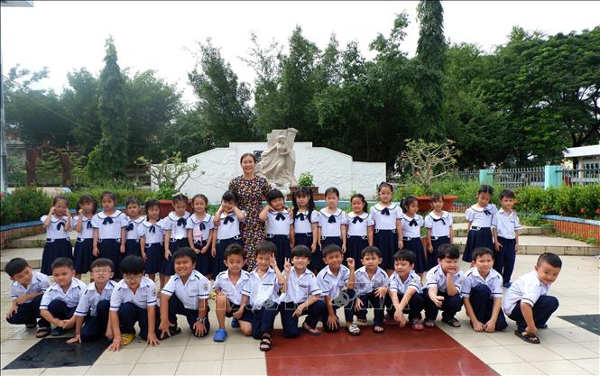 Nhà giáo ưu tú Trần Thị Thuý Hằng và học sinh lớp Một - 1 của mình bên tượng đài Anh hùng Mai Thị Non trong khuôn viên nhà trường. Ảnh: Đức Hạnh - TTXVN 