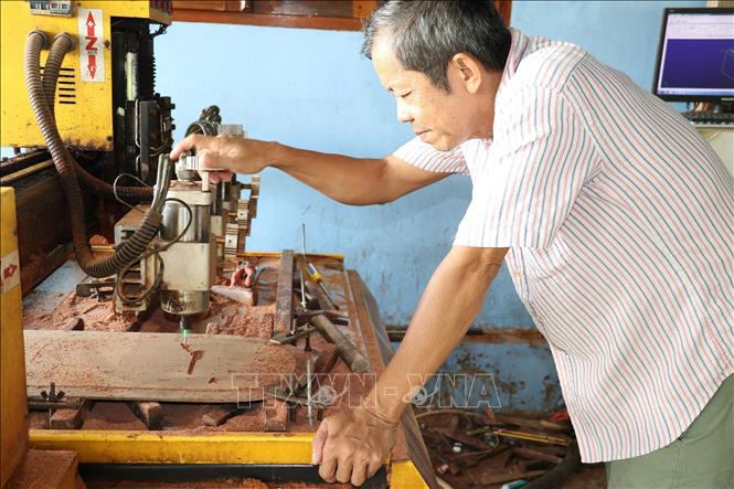 Ông Cao Văn Cận kiểm tra công đoạn đục hình trên thân gỗ bằng máy. Ảnh: Hữu Chí – TTXVN