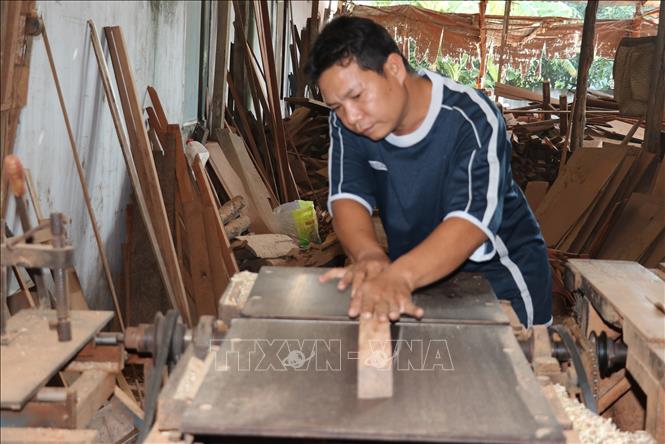 Anh Nguyễn Văn Thức bào gỗ để đóng tủ thờ. Ảnh: Hữu Chí – TTXVN