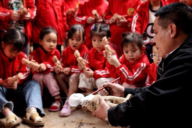 Nghệ nhân Nguyễn Văn Phi chế tác quân trò rối trước ánh mắt đầy tò mò, ngỡ ngàng, thán phục của những du khách nhỏ tuổi khi được đến tham quan làng múa rối Đào Thục. Ảnh: Phạm Hậu - TTXVN