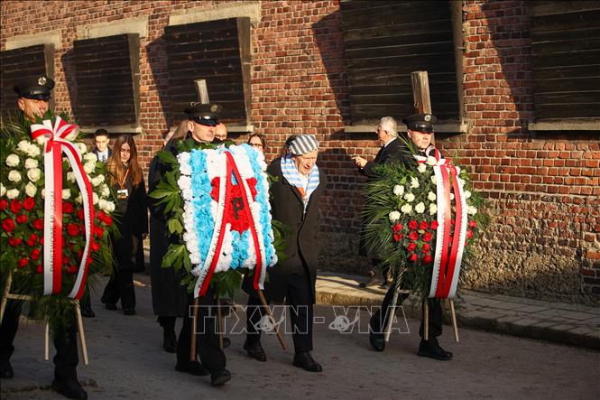 Các cựu tù nhân và khách mời đặt hoa tại Bức tường Tử thần của trại tập trung Auschwitz trong buổi lễ. Ảnh: PAP/TTXVN
