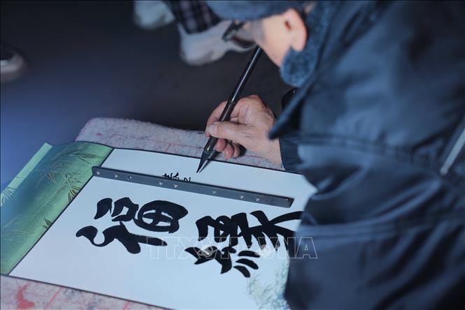 Những ông đồ, bà đồ (thường là những người cao tuổi có tài viết chữ đẹp) sẽ viết chữ cho khách với những nét chữ thư pháp thanh thoát, uyển chuyển. Ảnh: Hoàng Hiếu - TTXVN