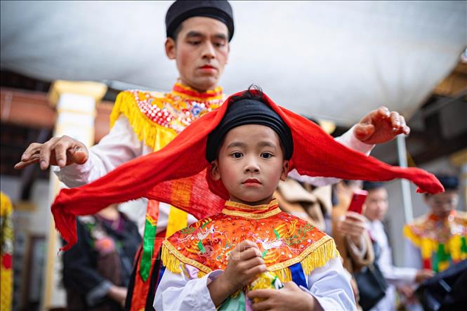 Thành viên CLB trống bồng Triều Khúc hỗ trợ chít khăn mỏ quạ cho em nhỏ. Ảnh: Phạm Tuấn Anh - TTXVN