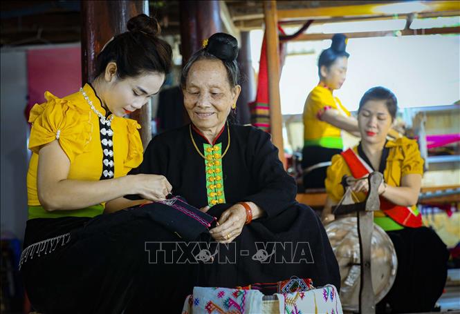 An experienced weaver teaches younger generations how to weave brocade fabrics. VNA Photo: Xuân Tư