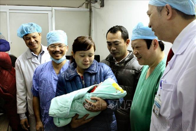 GS.TS Nguyễn Viết Tiến, Thứ trưởng Bộ Y tế (áo xanh, bên phải) - người trực tiếp phẫu thuật ca mang thai hộ đầu tiên tại Bệnh viện Phụ sản Trung ương cùng các bác sĩ chào đón bé gái đầu tiên ra đời từ phương pháp mang thai hộ (2016). Ảnh: Dương Ngọc – TTXVN