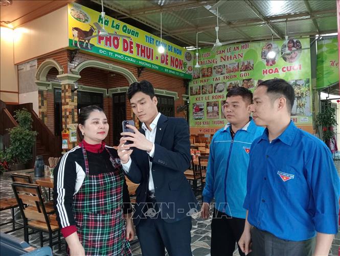 Đoàn viên thanh niên huyện Hương Sơn hướng dẫn người dân sử dụng các phương thức thanh toán không dùng tiền mặt. Ảnh: TTXVN phát