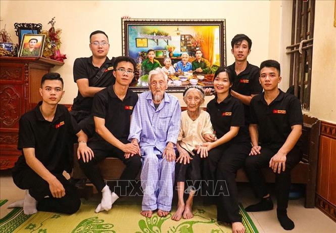Phùng Quang Trung (hàng trên, ngoài cùng, bên phải) cùng nhóm Skyline về thăm gia đình và trao tặng Mẹ Việt Nam anh hùng Nguyễn Thị Ngách bức ảnh mô phỏng bữa cơm đoàn viên cùng hai người con trai. Ảnh: TTXVN phát 