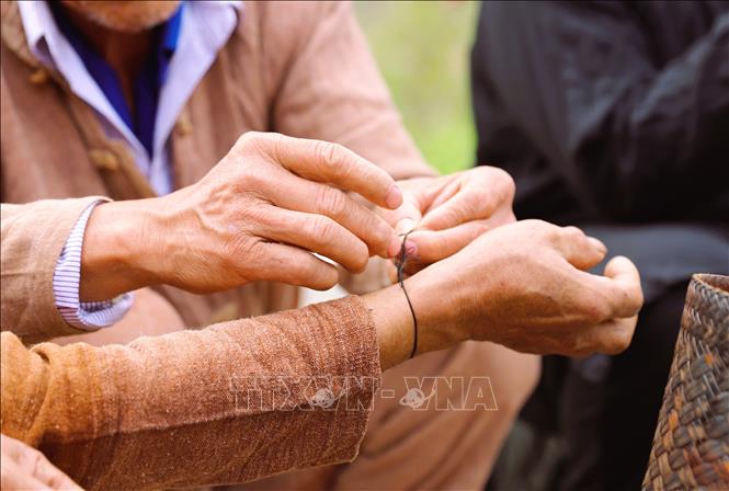 Nghi thức buộc chỉ ở cổ tay được thực hiện cho mọi người dân trong bản cạnh mâm cúng làm vía cho người dân với mong muốn người được cột chỉ luôn mạnh bạo, may mắn. Ảnh: Xuân Tiến - TTXVN 