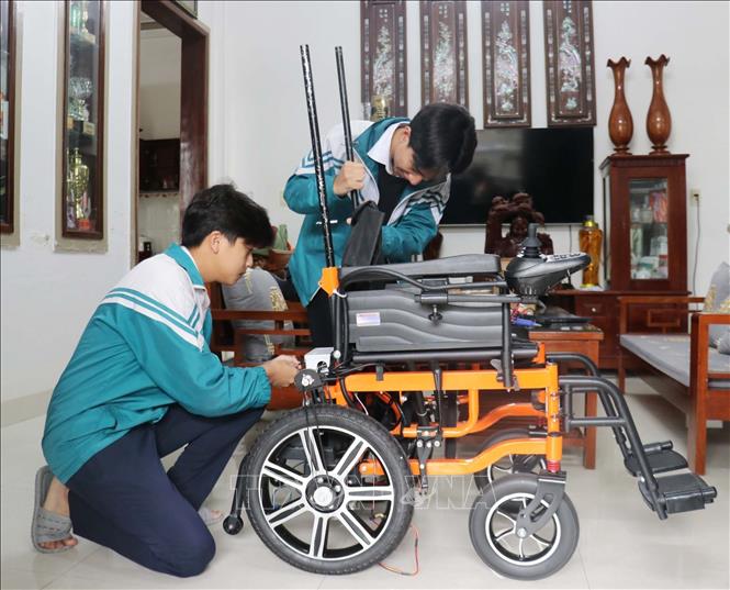 Em Cao Trung Quân và Lê Minh Hiếu lắp ráp chiếc xe lăn tự hành dành cho người bị mắc bệnh xơ cứng teo cơ. Ảnh: Thanh Thuỷ-TTXVN