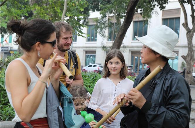 Foreign visitors experience bamboo flute on Hanoi's street. VNA Photo: Thành Phương