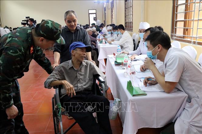 Tình nguyện viên hỗ trợ một người dân di chuyển bằng xe lăn ở thị trấn Đồng Đăng, huyện Cao Lộc, tỉnh Lạng Sơn đến bàn khám bệnh. Ảnh: Văn Đạt - TTXVN