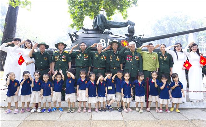Các cựu chiến binh và thế hệ trẻ chụp ảnh bên mô hình xe tăng tại Dinh Độc Lập. Ảnh: Hương Giang - TTXVN