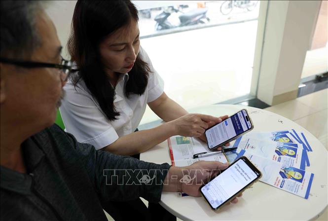 Nhân viên điện lực hướng dẫn người dân cài ứng dụng EVNNPC chăm sóc khách hàng, hỗ trợ mọi dịch vụ điện ở phòng giao dịch thành phố Thanh Hoá, tỉnh Thanh Hoá. Ảnh: Vũ Sinh – TTXVN