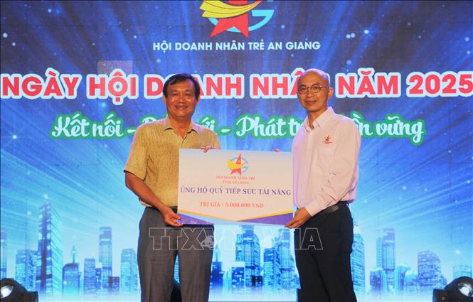 Anh Nguyễn Đình Luân, Phó Chủ tịch Hội Doanh nhân trẻ An Giang (phải) trao bảng tượng trưng hỗ trợ nguồn lực cho Quỹ tiếp sức tài năng tỉnh An Giang. Ảnh: Công Mạo-TTXVN