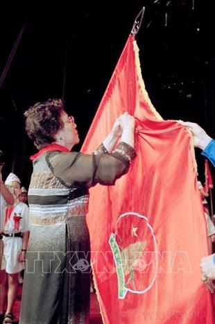 Phó Chủ tịch nước Nguyễn Thị Bình gắn Huân chương Sao vàng lên lá cờ truyền thống của Đội Thiếu niên Tiền phong Hồ Chí Minh (2001). Ảnh: Đình Trân - TTXVN