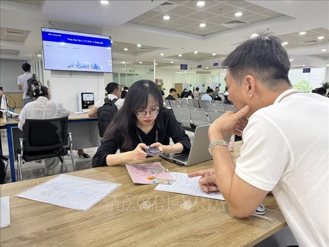 Cán bộ Trung tâm phục vị hành chính công hướng dẫn người dân lấy số thứ tự online đối với hồ sơ liên quan đến đất đai qua ứng dụng iHanoi. Ảnh: Quốc Lũy - TTXVN