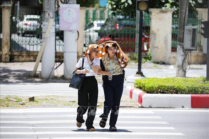 Hai người phụ nữ che chắn nắng khi băng qua đại lộ Thịnh Lang. Ảnh: Trọng Đạt - TTXVN