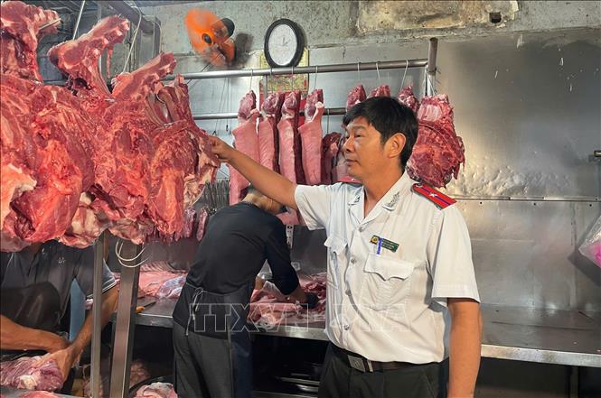 Cán bộ Đội quản lý an toàn thực phẩm số 9 kiểm tra cảm quan thịt lợn tại sạp pha lóc. Ảnh: Hương Giang - TTXVN