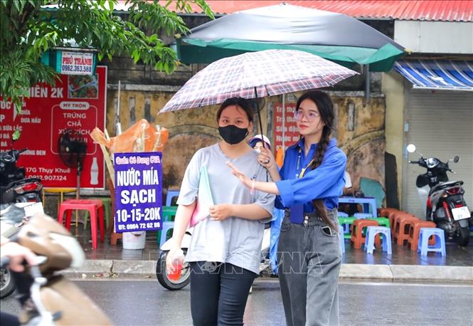 Thanh niên tình nguyện hỗ trợ thí sinh che mưa vào địa điểm thi trường THPT chuyên Chu Văn An (quận Tây Hồ, Hà Nội). Ảnh: Khánh Hoà - TTXVN
