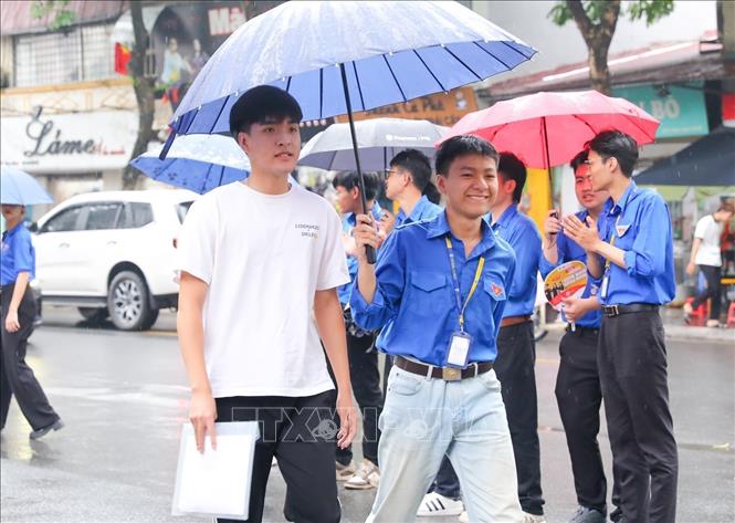 Thanh niên tình nguyện hỗ trợ thí sinh che mưa vào địa điểm thi trường THPT chuyên Chu Văn An (quận Tây Hồ, Hà Nội). Ảnh: Khánh Hoà - TTXVN
