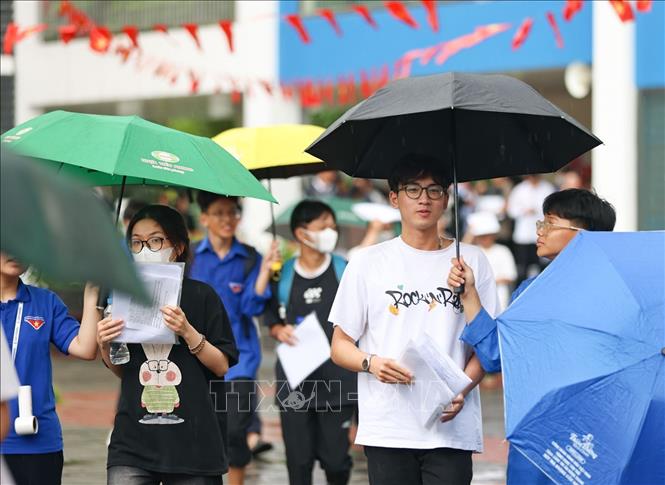 Tình nguyện viên hỗ trợ che ô đón thí sinh dưới mưa tại điểm thi trường THCS Lý Sơn, quận Long Biên (Hà Nội). Ảnh: Thanh Tùng - TTXVN