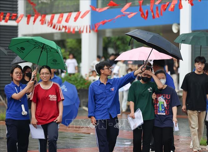 Tình nguyện viên hỗ trợ che ô đón thí sinh dưới mưa tại điểm thi trường THCS Lý Sơn, quận Long Biên (Hà Nội). Ảnh: Thanh Tùng - TTXVN