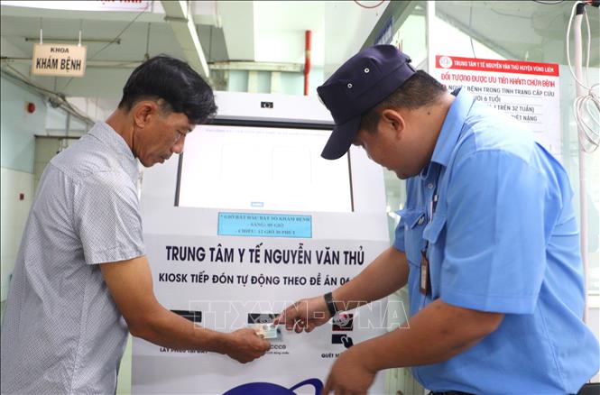 Hướng dẫn người dân thực hiện bốc số khám bệnh tự động tại Trung tâm Y tế Nguyễn Văn Thủ, huyện Vũng Liêm. Ảnh: Lê Thúy Hằng - TTXVN