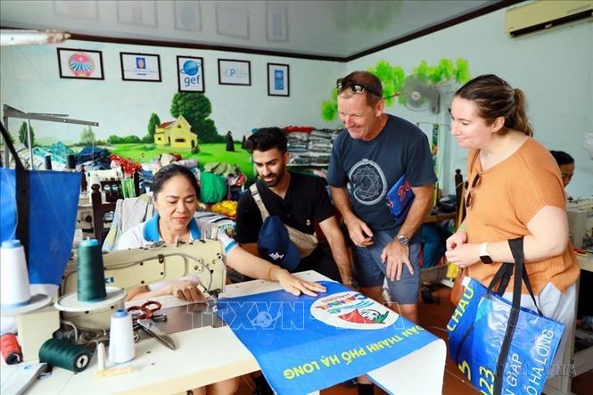 Khách nước ngoài xem quy trình may chiếc túi xách từ tấm pano bỏ đi tại Hợp tác xã Green Life Hạ Long (Quảng Ninh). Ảnh: Đức Hiếu - TTXVN