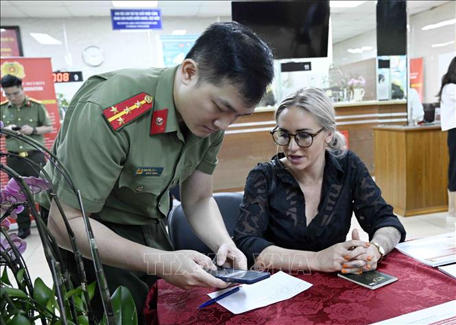 Cán bộ, chiến sĩ Cục quản lý xuất nhập cảnh, Bộ Công an hướng dẫn người nước ngoài làm thủ tục cấp tài khoản định danh điện tử. Ảnh: Phạm Kiên - TTXVN