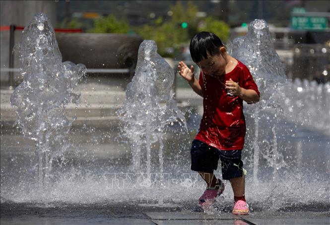 Em nhỏ chơi đùa bên đài phun nước để tránh nóng, tại Seoul, Hàn Quốc. Ảnh: THX/TTXVN