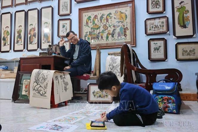 Nghệ nhân ưu tú Nguyễn Hữu Quả, thế hệ thứ 13 làm tranh Đông Hồ, vui mừng khi cháu nội thích thú vẽ với các khung hình Đông Hồ cổ (2025). Ảnh: Hoàng Hiếu - TTXVN