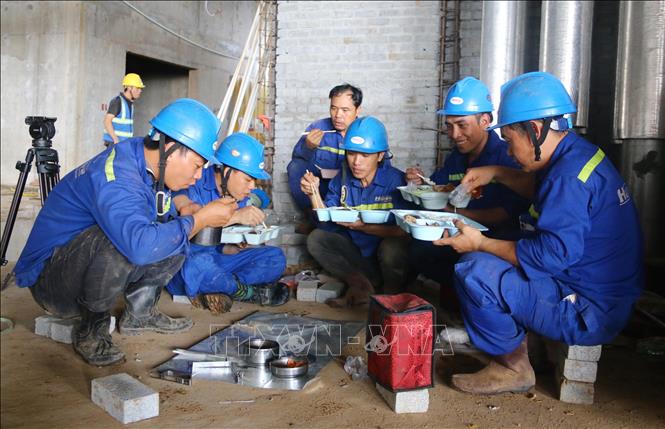 Công nhân tranh thủ ăn cơm trưa ngay tại công trường. Ảnh: Công Phong - TTXVN