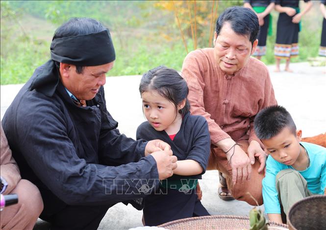 Thấy cúng, già làng, người có uy tín thực hiện nghi thức buộc chỉ cổ cổ tay, đặt tên và làm vía cho người dân để mong muốn người được cột chỉ cổ tay luôn khỏe mạnh, gặp nhiều niềm vui, may mắn. Ảnh: Xuân Tiến - TTXVN 