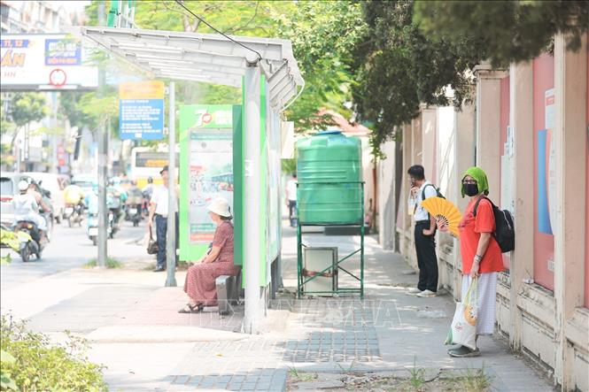 Quạt, khăn ướt phủ đầu...là cách của người dân chọn khi đợi xe buýt. Ảnh: Lê Đông - TTXVN