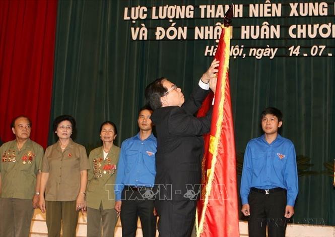 Chủ tịch nước Nguyễn Minh Triết gắn huân chương Sao Vàng lên lá cờ truyền thống của lực lượng Thanh niên xung phong Việt Nam tại Lễ kỷ niệm 60 năm Ngày thành lập lực lượng (15/7/1950 - 15/7/2010). Ảnh: Nguyễn Khang - TTXVN 