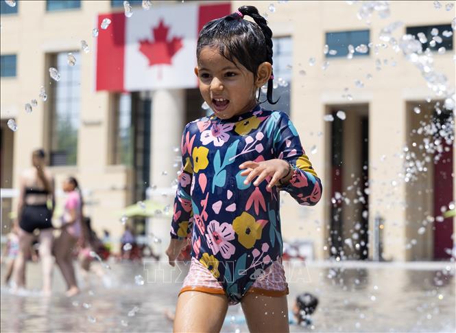 Em nhỏ chơi đùa bên đài phun nước để tránh nóng tại Toronto, Canada. Ảnh: THX/TTXVN