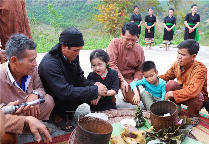 Các cháu nhỏ được thầy mo (thầy cúng) và các già làng, trưởng bản, người có uy tín buộc chỉ vào cổ tay và nhập họ, chính thức đặt tên sau khi lễ cúng làm vía cho bản làng kết thúc. Ảnh: Xuân Tiến - TTXVN 
