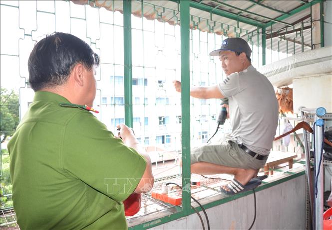 Công an hướng dẫn thợ làm cửa sắt đảm bảo an toàn phòng cháy khi tháo dỡ “chuồng cọp”. Ảnh: Linh Sơn-TTXVN
