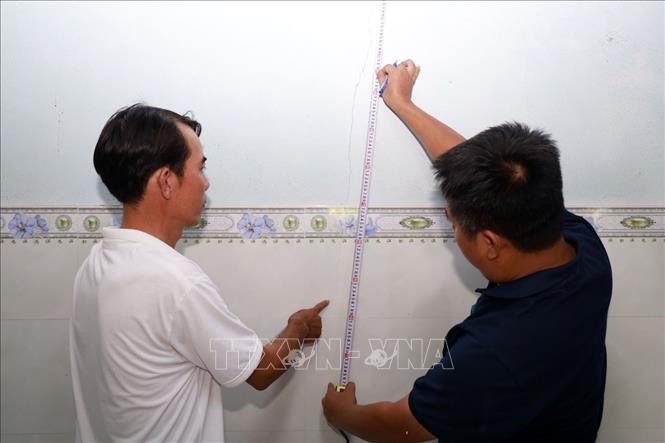 Bộ phận giám định để bồi thường thiệt hại cùng với hộ dân đo kích thước vết nứt. Ảnh: Xuân Triệu - TTXVN