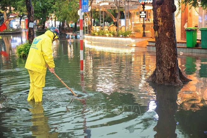 Công nhân thoát nước Hà Nội đang khơi thông dòng chảy tại điểm ngập trên phố Lê Thái Tổ. Ảnh: Hoàng Hiếu - TTXVN
