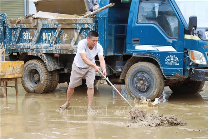 Người dân dọn bùn đất trước nhà ở. Ảnh: Xuân Tiến - TTXVN 