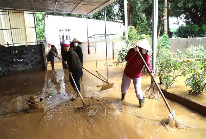 Người dân hỗ trợ, giúp nhau đẩy hàng khối bùn, đất bẩn ra khỏi sân nhà. Ảnh: Xuân Tiến - TTXVN 