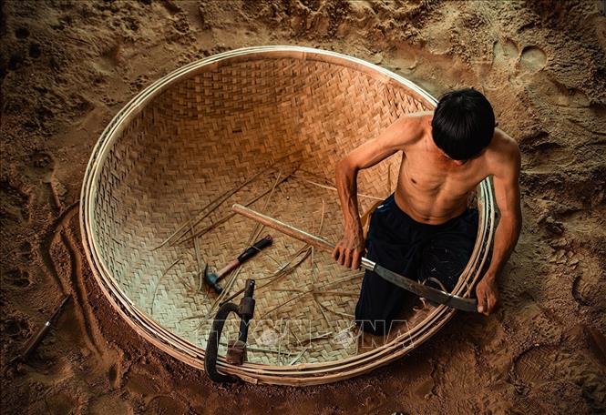 Người thợ đào hầm đất làm khuôn rồi đặt nguyên tấm mê thúng đã đan xong xuống hầm. Công đoạn lận vành là một trong những công đoạn quan trọng quyết định đến chất lượng sản phẩm để chiếc thúng sau khi lận cả vòng thúng và vành phải tròn đều, cân bằng và không biến dạng”. Ảnh: Khánh Hòa – TTXVN