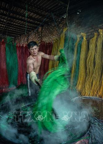 Sợi cói phải được nhúng đều vào nước nhuộm đang đun sôi để giữ được màu tươi lâu hơn. Ảnh: Khánh Hoà – TTXVN 
