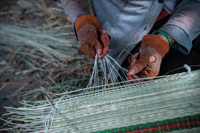 Tỉ mỉ buộc những sợi dây dù trắng quanh mép chiếu. Ảnh: Khánh Hoà – TTXVN 