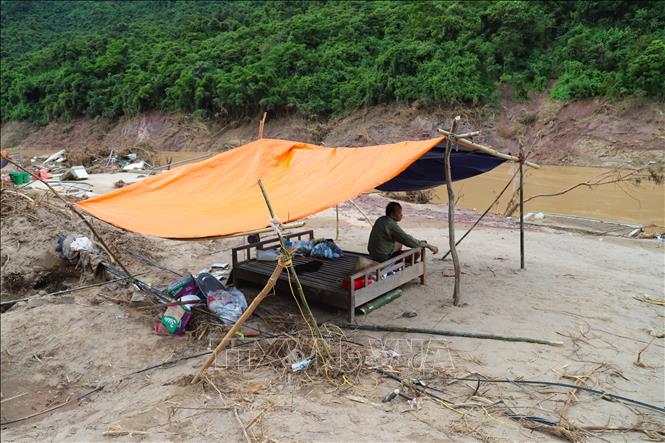 Người đàn ông ngồi thất thần nhìn đống đổ nát trong căn lều dựng tạm bợ trên nền một ngôi nhà xây đã bị lũ cuốn trôi. Ảnh: Xuân Tiến - TTXVN 
