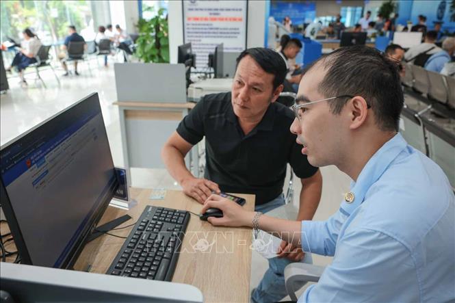 Nhân viên Bưu điện Hà Nội Nguyễn Thanh Tâm hỗ trợ ông Đặng Đức Hòa, phường Cửa Nam đến làm hồ sơ dịch vụ vận tải tại Trung tâm phục vụ hành chính công Thành phố Hà Nội - chi nhánh số 1. Ảnh: Hoàng Hiếu - TTXVN