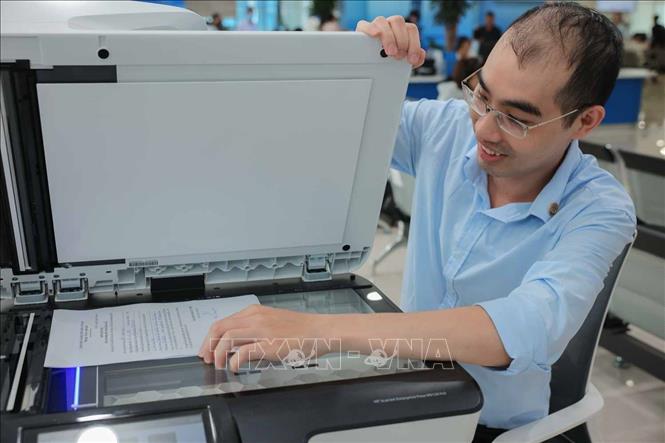 Anh Nguyễn Thanh Tâm (nhân viên Bưu điện Hà Nội) hỗ trợ scan tài liệu - hồ sơ số hóa cho công dân tại Trung tâm phục vụ hành chính công Thành phố Hà Nội - chi nhánh số 1. Ảnh: Hoàng Hiếu - TTXVN