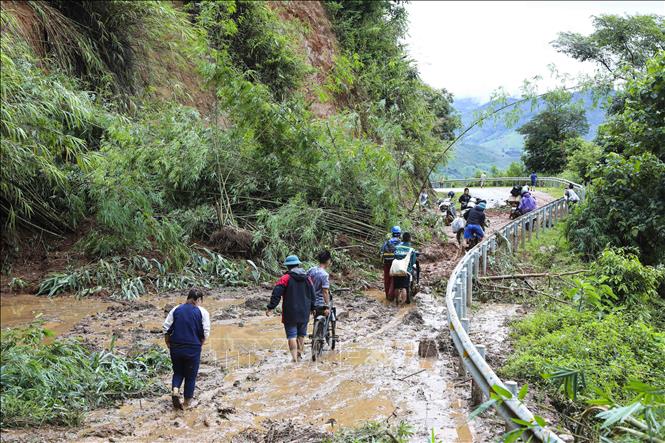 Người và xe máy vất vả di chuyển qua các điểm sạt lở. Ảnh: TTXVN